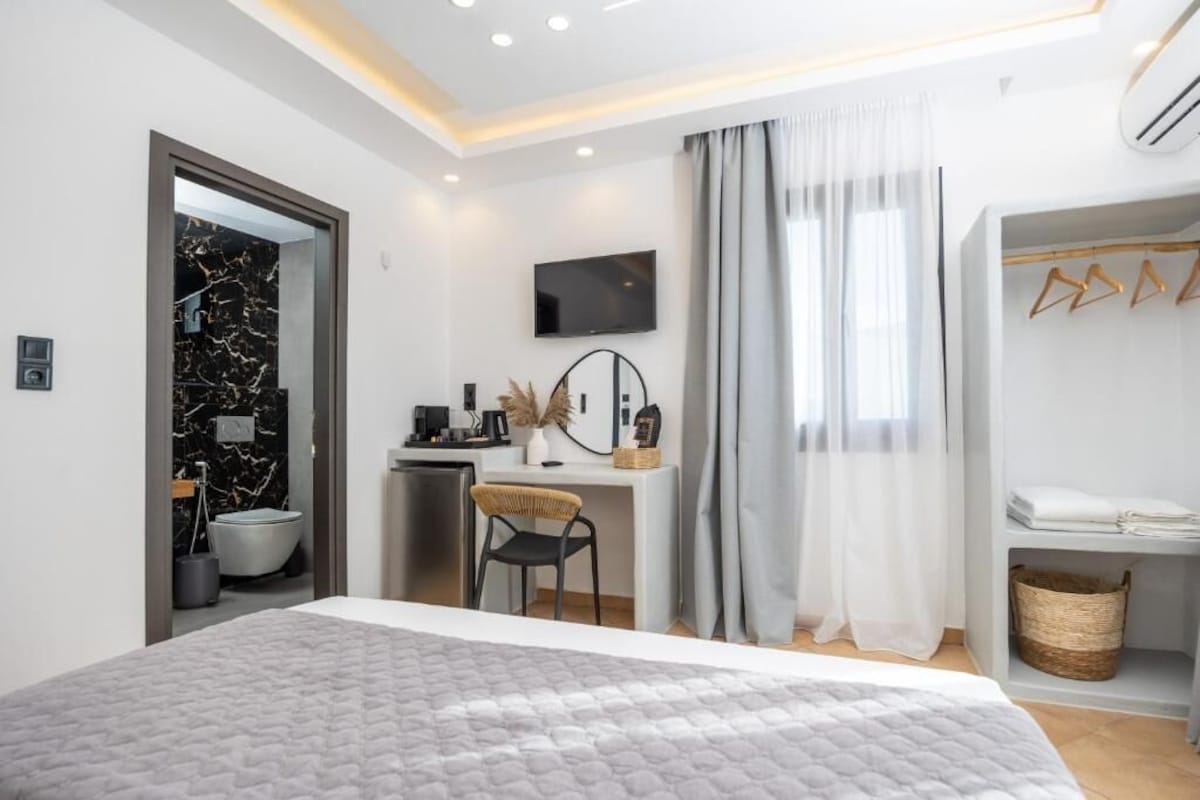 Quarto de hotel moderno com uma cama grande, escrivaninha, televisão e banheiro.