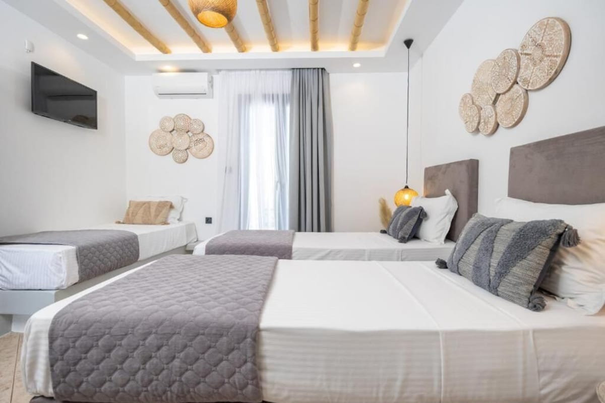 Quarto de hotel moderno com duas camas, televisão de tela plana, arte decorativa na parede e uma janela grande com cortinas.