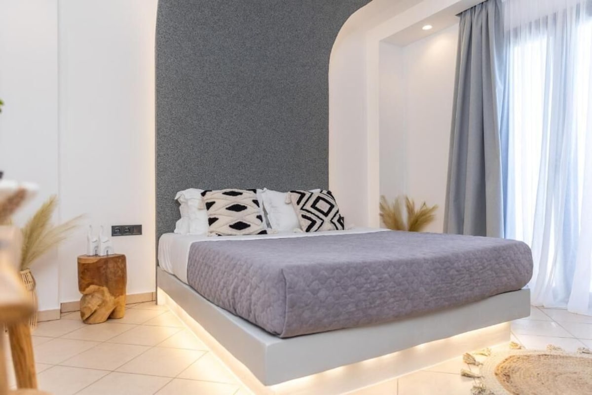 Quarto moderno com cama, mesas de cabeceira e vista para o exterior.