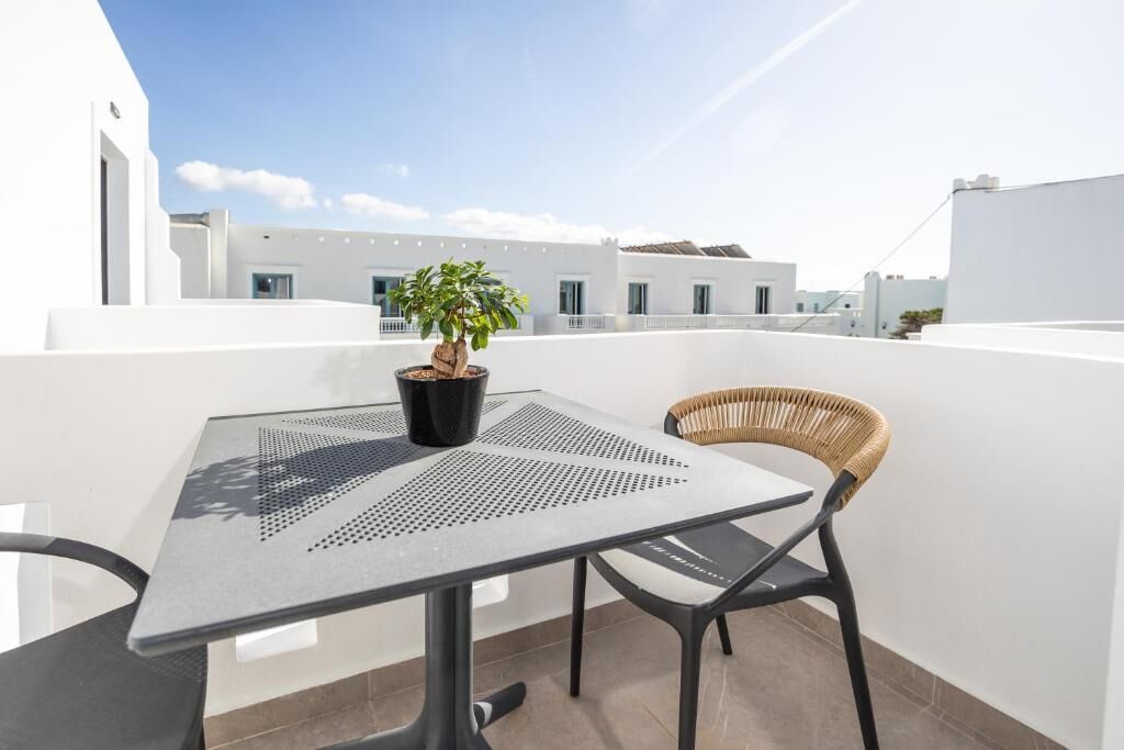 A rooftop terrace with a table, a chair, a potted plant, and a view of white buildings.