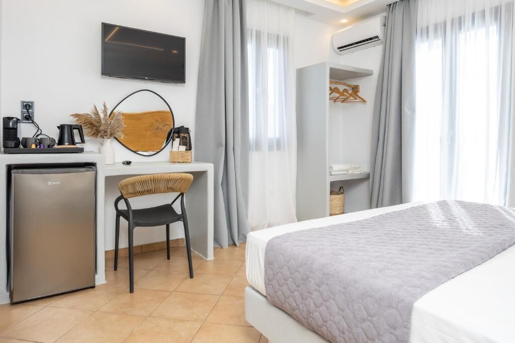 A hotel room with a bed, a desk with a chair, a television, a refrigerator, and a wardrobe.