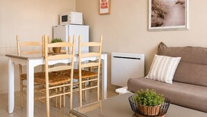 Un soggiorno con un tavolino in vetro, un divano, un tavolo da pranzo con sedie, una lampada a sospensione, un quadro incorniciato e una piccola pianta sul tavolo.