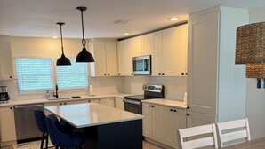 Une cuisine moderne avec des meubles blancs, un îlot central, des tabourets de bar bleus et une table à manger avec des chaises blanches.