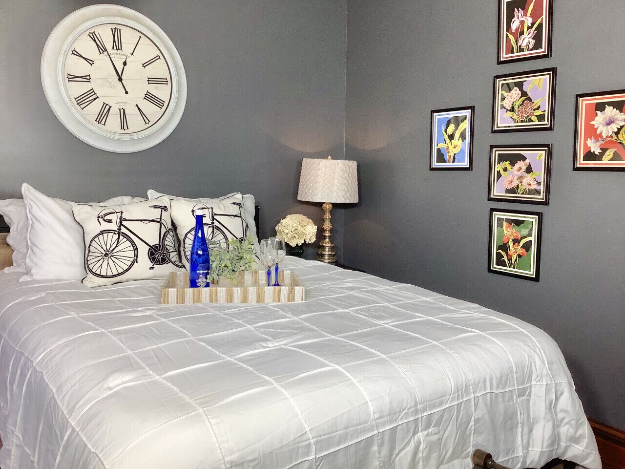 Ein Schlafzimmer mit einem Bett, einer Wanduhr, gerahmten Bildern, einer Lampe und Dekorationselementen.