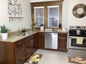Una cocina con armarios de madera, lavavajillas de acero inoxidable, horno y un reloj de pared decorativo.