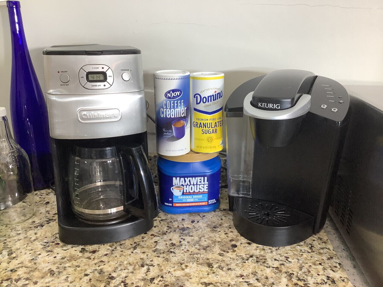Una encimera de cocina con una cafetera Cuisinart, una Keurig y dos latas de crema para café.