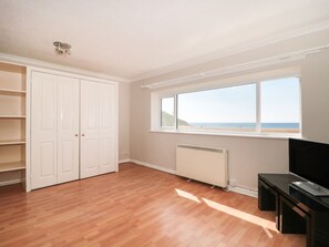 A room with a large window, wooden flooring, a white wardrobe, and a black TV stand. - Flat 30 (Bridport)