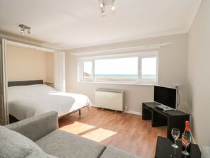 Un dormitorio con cama, televisión, ventana con vista a la playa y una mesita con vasos.