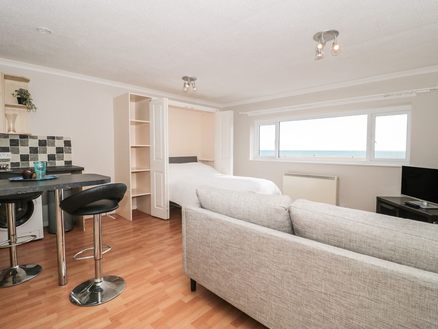 A compact room with a bed, a sofa, a dining area with a table and chairs, and a TV.