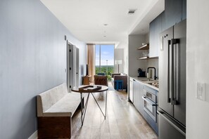 Eine moderne Küche mit einem großen Kühlschrank, eine Essecke mit einer Bank und einem Tisch sowie ein Blick auf Grünflächen.