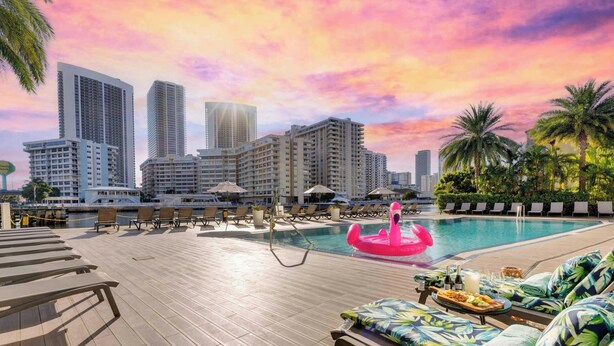 Ett poolområde på taket med solstolar, en rosa uppblåsbar badleksak och stadens silhuett i bakgrunden.