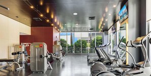Ein Fitnessraum mit Cardiogeräten, Gewichten und großen Fenstern mit Blick ins Freie.