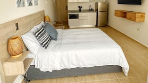 Un dormitorio con cama, mesita de noche, televisor montado en la pared y una pequeña cocina.
