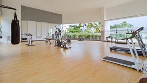 Un gimnasio espacioso con diversos equipos de ejercicio, ventanas amplias y vistas a zonas verdes.