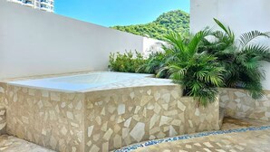 Una terraza en la azotea con una bañera de piedra, vegetación y vistas a una colina.