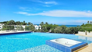 Una piscina azul cristalina con un jacuzzi, rodeada de exuberante vegetación y vistas al océano.