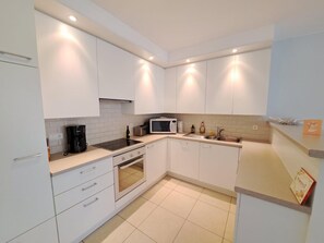 Eine moderne Küche mit weißen Schränken, einem eingebauten Backofen, einer Mikrowelle und einer Kaffeemaschine.