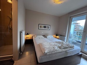 Ein Schlafzimmer mit Bett, Nachttischen, einem gerahmten Bild, einem Fenster mit Aussicht und einer Duschkabine.