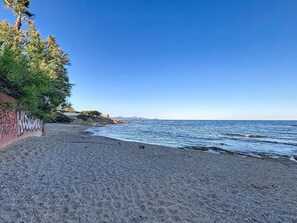 A beach with a rocky shoreline, a clear blue sky, and a building with graffiti on the left. - Le Victoria by Interhome (Saint Aygulf)