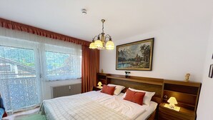 Un dormitorio con una cama grande, un cuadro en la pared, una ventana con cortinas y vistas al exterior.