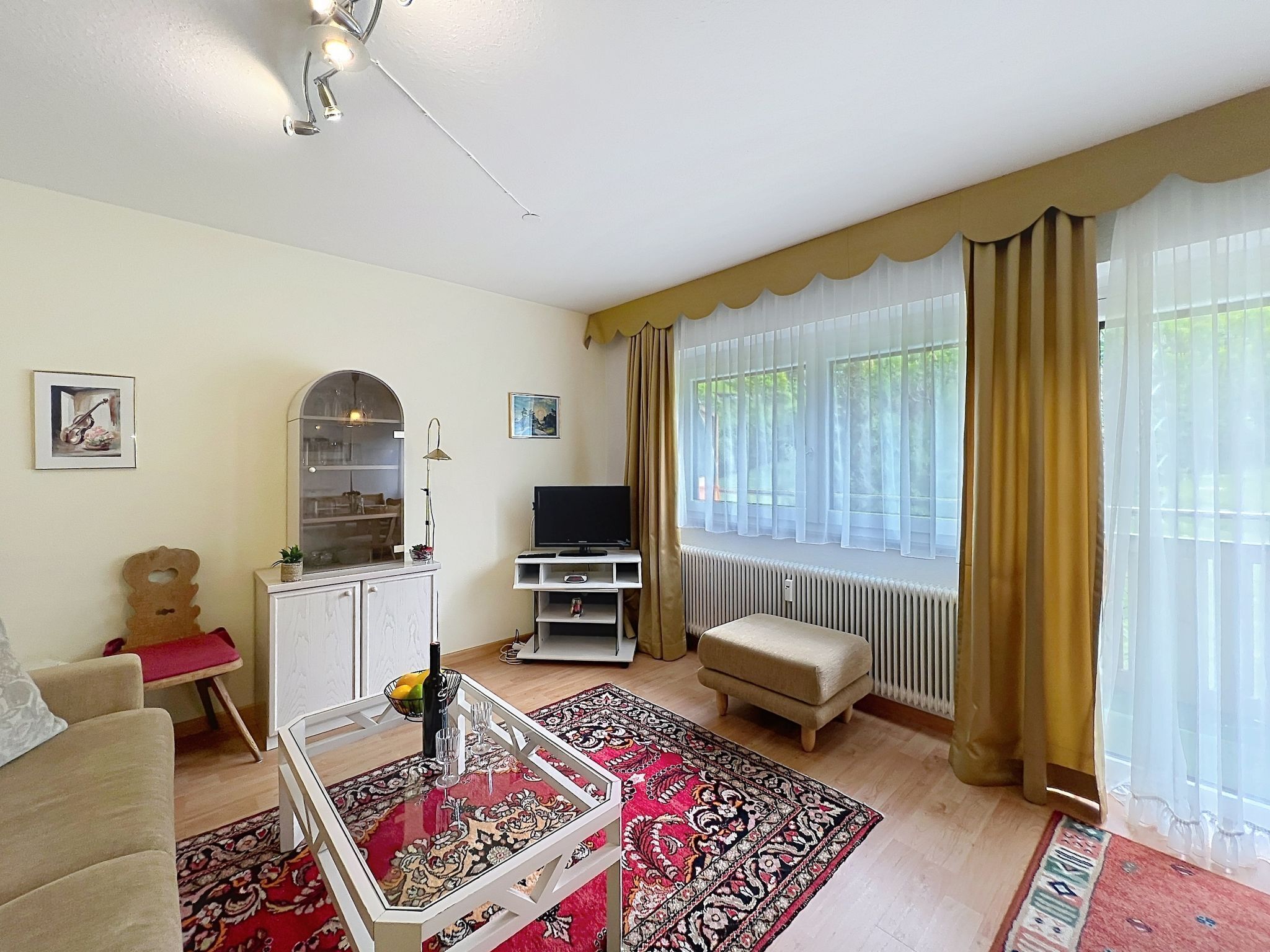 A living room with a sofa, a glass-top coffee table, a television, a cabinet, and a window with curtains.