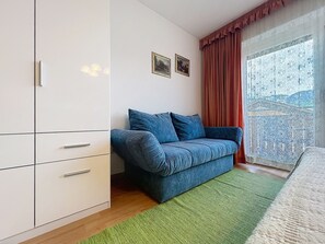 A bedroom with a white wardrobe, a blue sofa, a green rug, and a window with a view.