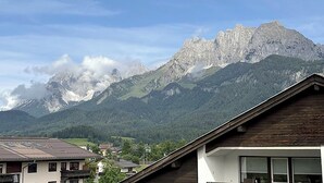 Un paisaje montañoso con un pico destacado, una zona residencial con casas y una construcción de madera con techo inclinado.