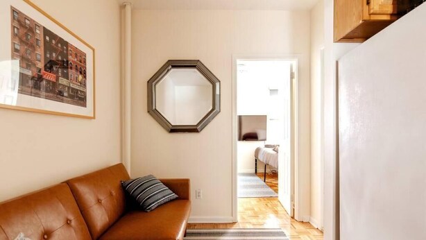 Una sala de estar con un sofá de cuero marrón, un tapete a rayas, un cuadro enmarcado en la pared y un espejo hexagonal.