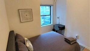 Un dormitorio con cama, escritorio y ventana.