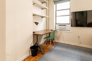 Quarto com escrivaninha, cadeira, janela, televisão e radiador.