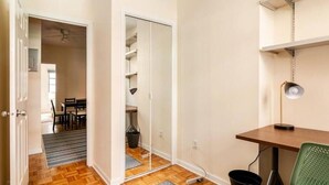Una habitación con piso de madera, un escritorio con lámpara, una silla verde y un armario con estantes.