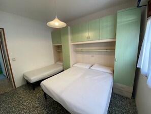 Ein Schlafzimmer mit zwei Einzelbetten, einem grünen Kleiderschrank und einer Pendelleuchte.