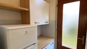 A compact kitchen with white cabinets, a white refrigerator, a wooden countertop, and a frosted glass door. - Ground Floor Apartment Near Beach (San Michele al Tagliamento)