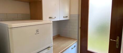 A compact kitchen with white cabinets, a white refrigerator, a wooden countertop, and a frosted glass door.