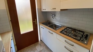 A kitchen with white cabinets, a stainless steel sink, and a gas stove. - Ground Floor Apartment Near Beach (San Michele al Tagliamento)