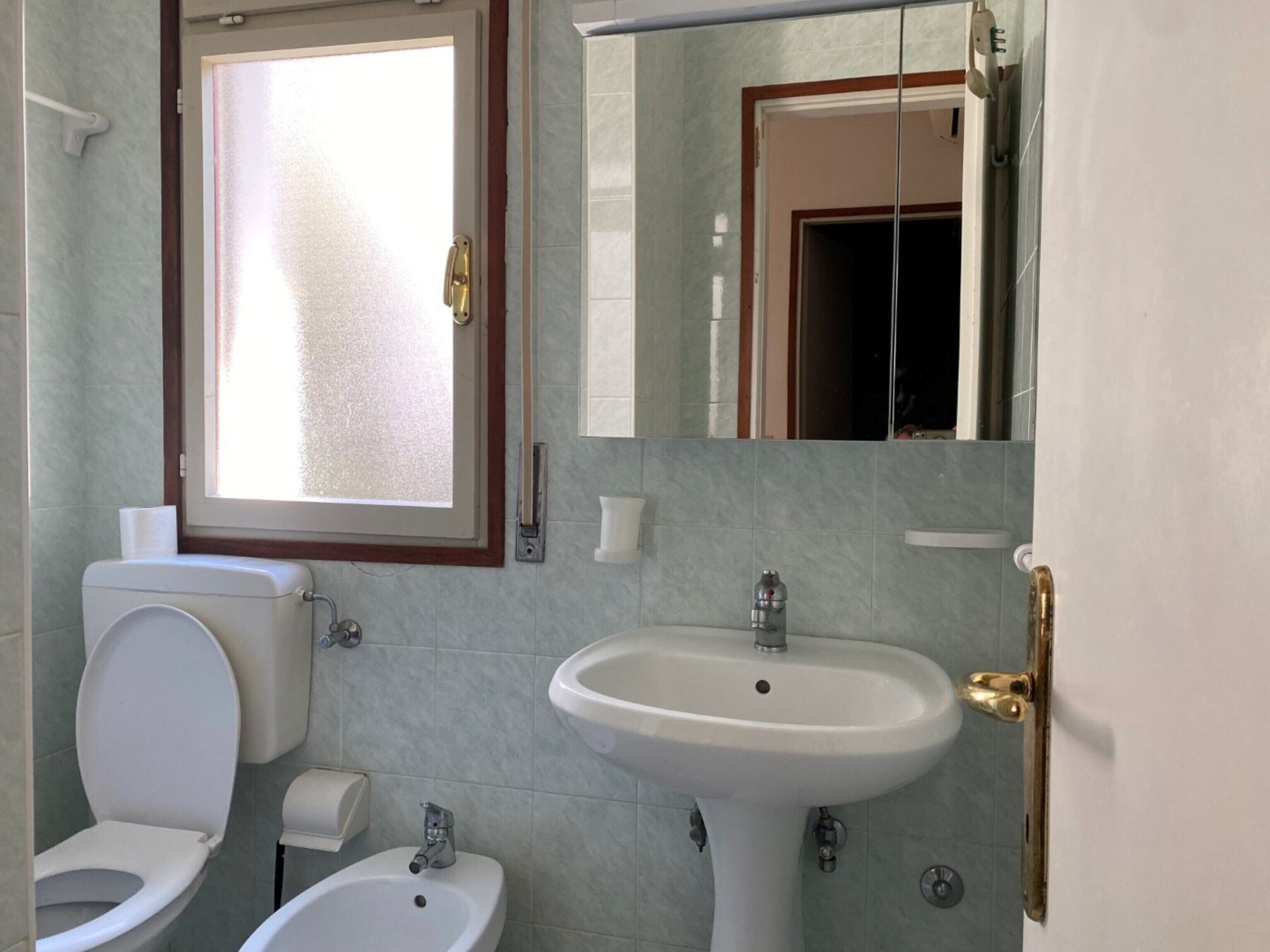 Een badkamer met toilet, bidet, wastafel en spiegel.