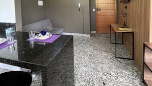 Una habitación moderna con suelo de mármol, puerta de madera, una pequeña mesa con una silla y un televisor montado en la pared.