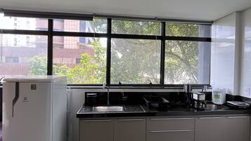 Cocina con refrigerador, lavamanos y ventana que da a edificios y árboles.