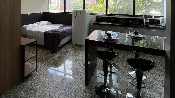 Una habitación compacta con cama, kitchenette y comedor con taburetes.