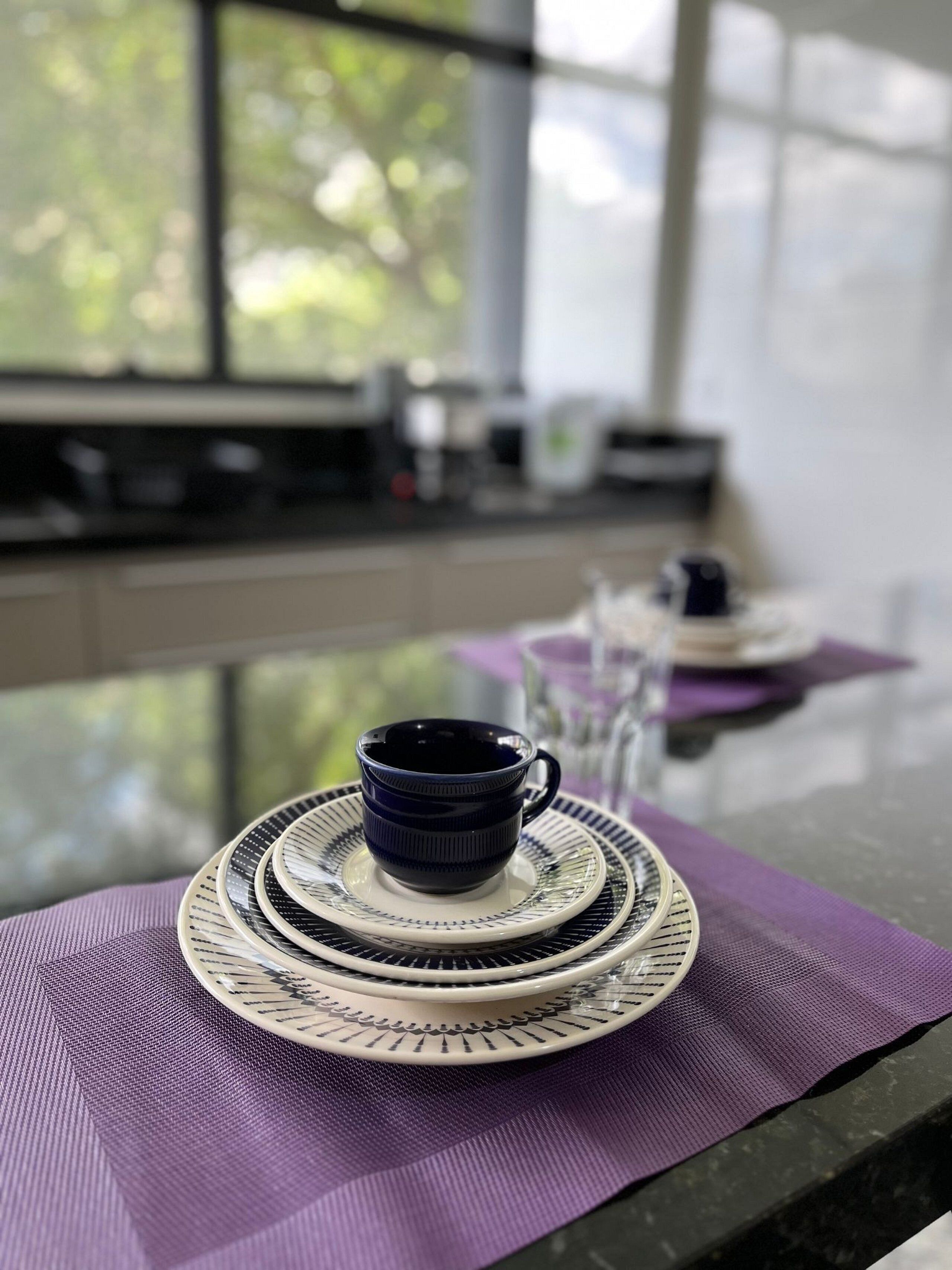 Ein Tisch mit einer blauen Tasse und Untertasse, einem weißen Teller und einer violetten Tischmatte.