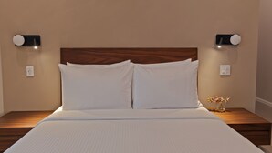 A bed with white linens, a wooden headboard, two bedside lamps, and a small vase with flowers on the nightstand. - Sosuite | Queen Room, High Floor w Desk, Roof Deck (Philadelphia)