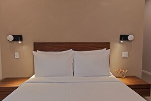 Ein Bett mit weißen Leinen, einem Holzkopfende, zwei Nachttischlampen und einer kleinen Vase mit Blumen auf dem Nachttisch.