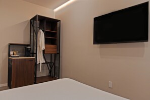 A bedroom with a bed, a TV mounted on the wall, a wardrobe, and a small table with a kettle.
