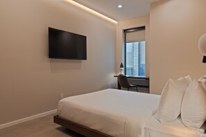 Ein modernes Hotelzimmer mit Bett, Schreibtisch, Stuhl, Flachbildfernseher und einem Fenster mit Stadtblick.