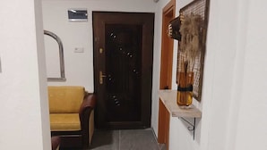 Un couloir avec un sol carrelé, une porte en bois, un canapé jaune et une étagère sur laquelle se trouve un vase.