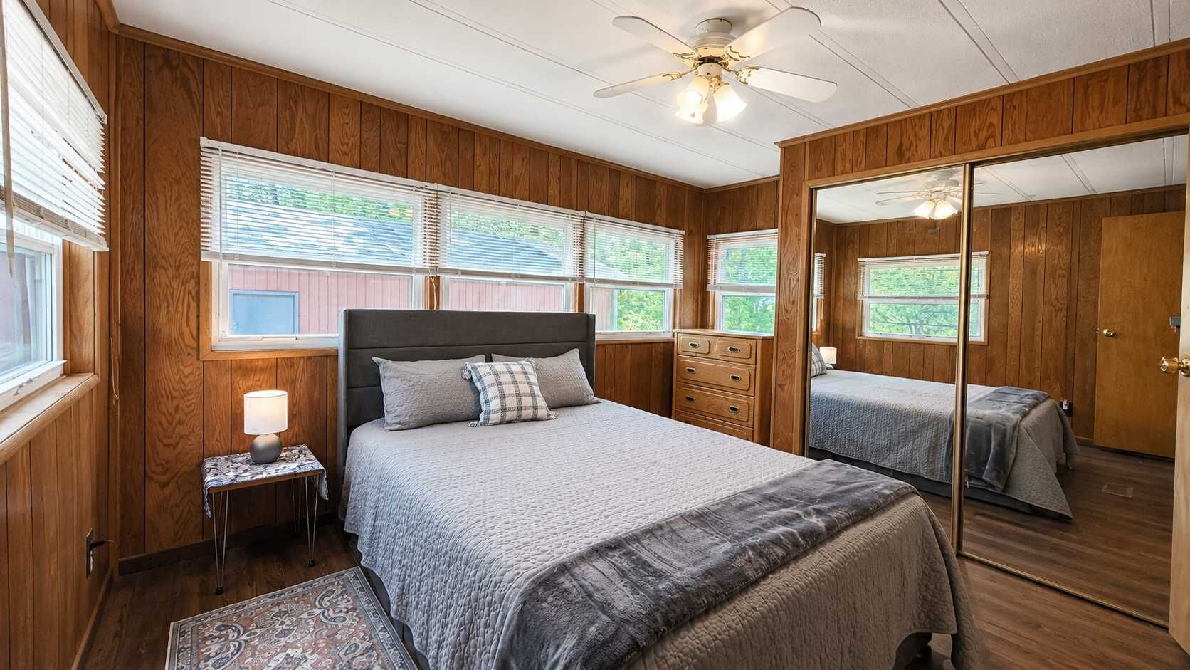 A bedroom with a bed, bedside table, mirror, and wooden walls.