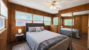 Ein Schlafzimmer mit Bett, Nachttisch, Spiegel und Holzwänden.