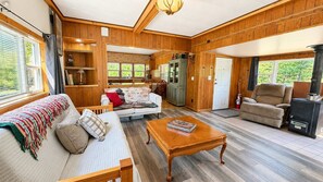 Ein gemütliches Blockhaus-Interieur mit Wohnzimmer, Sofa, Couchtisch, Kamin und Küchenzeile.