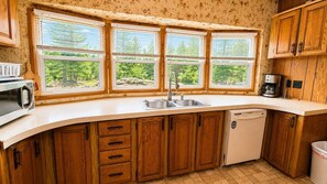 Eine Küche mit Holzausstattung, einer Spüle, einem Geschirrspüler und einem Fenster mit Blick auf Bäume.