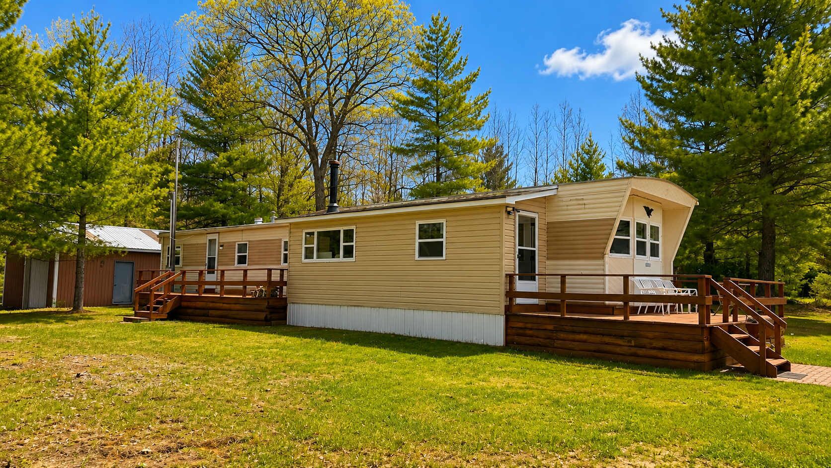 Une maison mobile de plain-pied avec une terrasse à l’avant, un petit garage attenant et une cour clôturée.